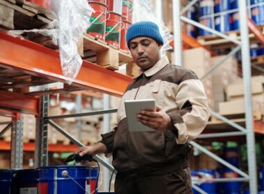 A man holding a tablet in a warehouse thinking about the top benefits of AI in logistics.