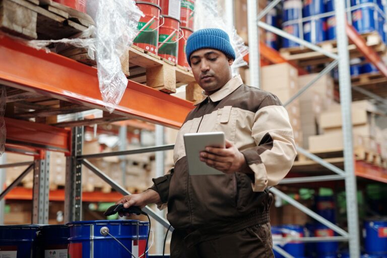 A man holding a tablet in a warehouse thinking about the top benefits of AI in logistics.